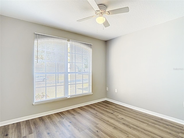empty room featuring a textured ceiling, wood finished floors, ceiling fan, and baseboards