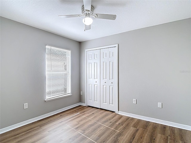 unfurnished bedroom featuring wood finished floors, baseboards, a ceiling fan, and a closet