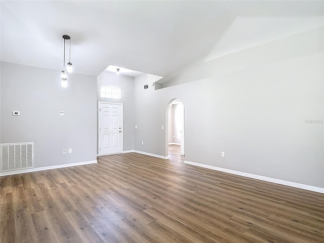 unfurnished living room featuring arched walkways, visible vents, wood finished floors, and baseboards