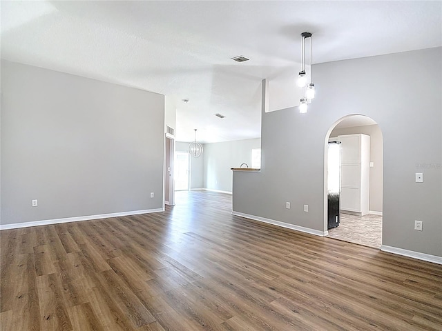 unfurnished room featuring lofted ceiling, visible vents, baseboards, arched walkways, and wood finished floors