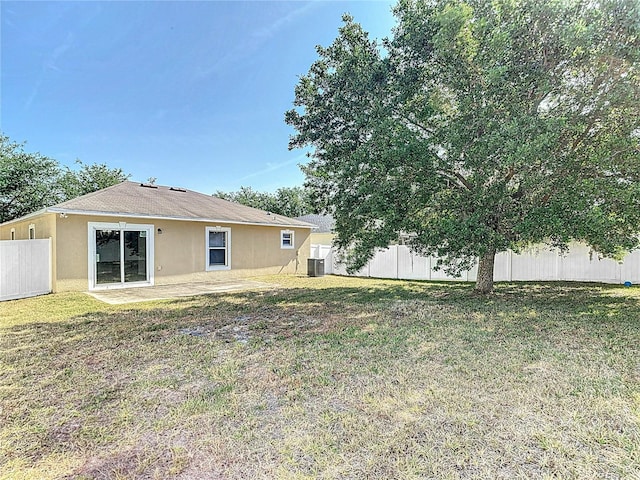 rear view of house featuring central AC, fence, stucco siding, and a lawn