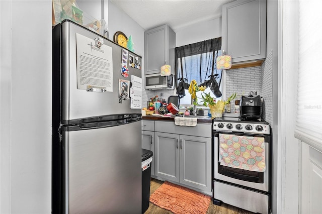 2134 6th Ave N, Saint Petersburg, FL 33713 - kitchen featuring dark countertops, light wood-type flooring, gray cabinets, appliances with stainless steel finishes, and backsplash