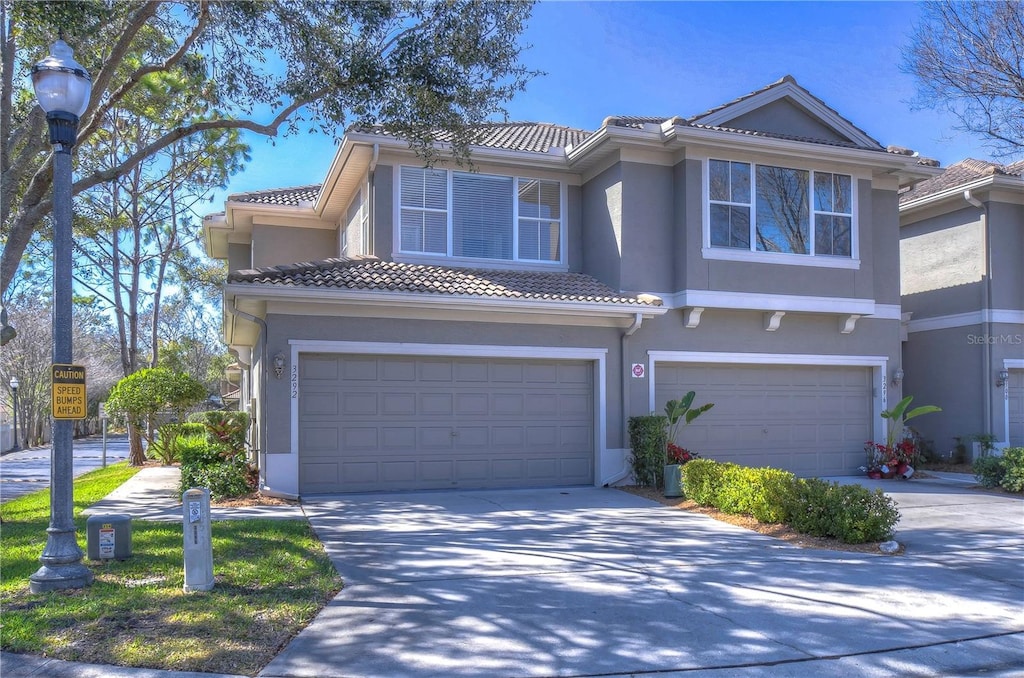 3292 Covered Bridge Dr E, Dunedin, FL 34698 - view of front of home featuring a tiled roof, an attached garage, concrete driveway, and stucco siding