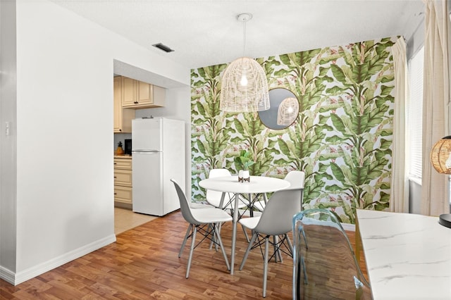 dining space with light wood-type flooring, visible vents, and baseboards