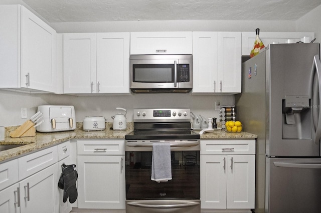 kitchen with light stone countertops, stainless steel appliances, and white cabinetry
