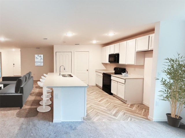 kitchen featuring a kitchen island with sink, baseboards, white cabinets, a sink, and black appliances