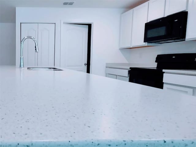 kitchen featuring white cabinetry, visible vents, a sink, and black appliances