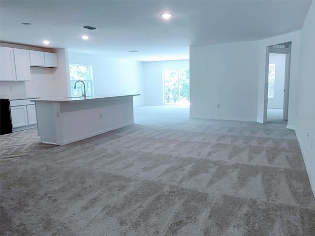 unfurnished living room featuring visible vents, a sink, baseboards, light carpet, and recessed lighting