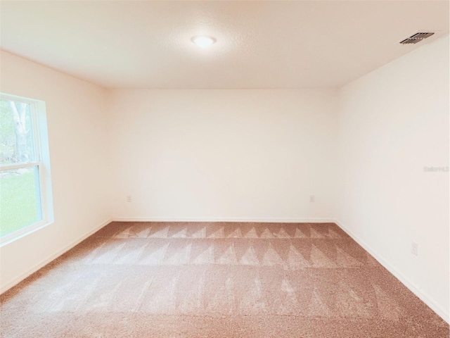 carpeted spare room with baseboards, a wealth of natural light, and visible vents