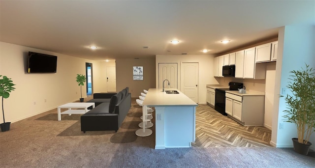kitchen featuring a kitchen island with sink, recessed lighting, light countertops, a sink, and black appliances