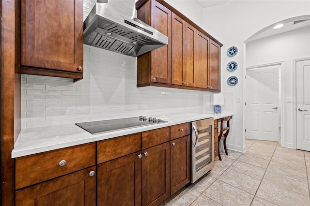 kitchen featuring beverage cooler, arched walkways, black electric cooktop, wall chimney exhaust hood, and tasteful backsplash