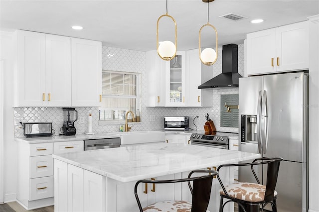kitchen featuring white cabinetry, a sink, stainless steel appliances, a kitchen island, and wall chimney exhaust hood