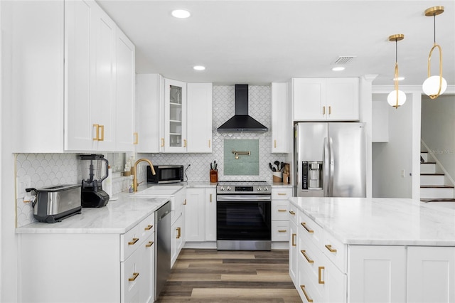 kitchen with wall chimney range hood, a sink, visible vents, stainless steel appliances, and wood finished floors