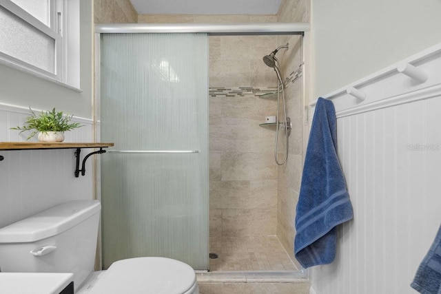 full bath with a decorative wall, toilet, wainscoting, and a stall shower