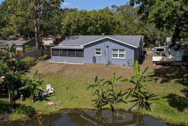 rear view of property featuring fence, roof with shingles, stucco siding, a sunroom, and a lawn
