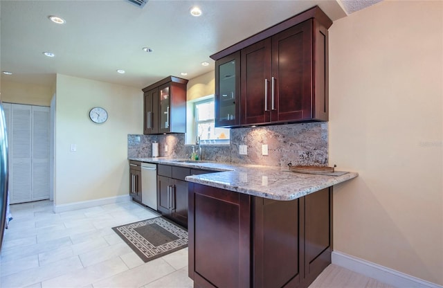kitchen with light stone countertops, a sink, decorative backsplash, baseboards, and stainless steel dishwasher