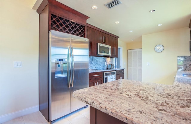 kitchen with light stone counters, decorative backsplash, appliances with stainless steel finishes, visible vents, and dark brown cabinets