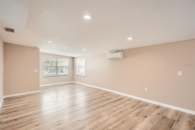 basement with an AC wall unit, visible vents, recessed lighting, and light wood-style floors