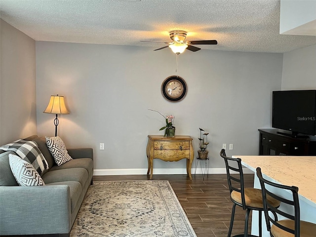 living room featuring ceiling fan, a textured ceiling, baseboards, and dark wood-type flooring