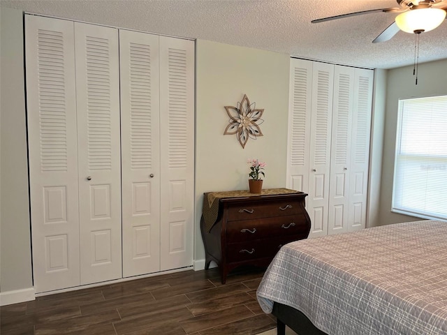 bedroom featuring multiple closets, dark wood finished floors, a textured ceiling, baseboards, and ceiling fan