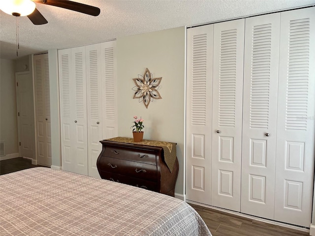 bedroom featuring a textured ceiling, two closets, dark wood-style flooring, ceiling fan, and baseboards