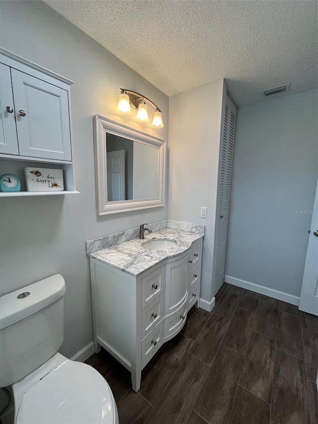 bathroom with wood tiled floor, a textured ceiling, toilet, visible vents, and vanity