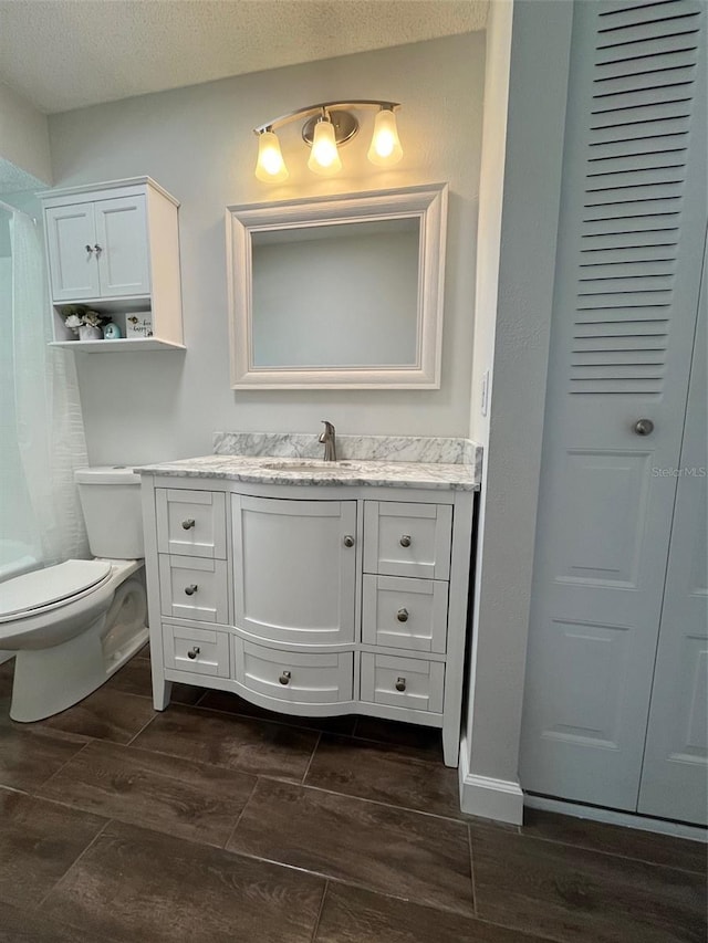 full bath featuring toilet, vanity, curtained shower, a textured ceiling, and wood tiled floor