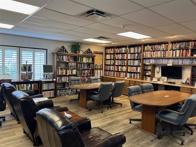 home office with a paneled ceiling, bookshelves, light wood-style flooring, and visible vents