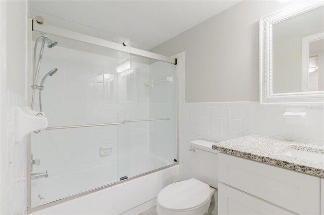 2457 Ecuadorian Way Unit 63, Clearwater, FL 33763 - bathroom with tile walls, a wainscoted wall, bath / shower combo with glass door, vanity, and toilet