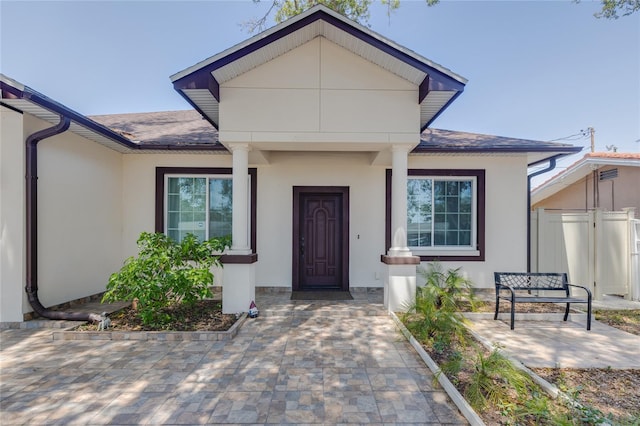 entrance to property featuring a shingled roof, stucco siding, and fence