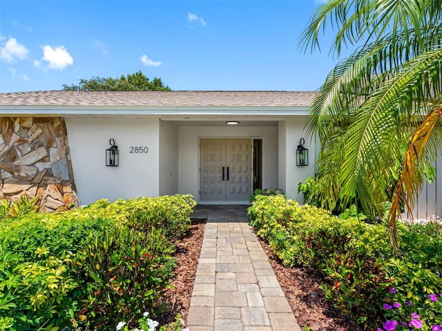 entrance to property featuring roof with shingles, stucco siding, and stone siding