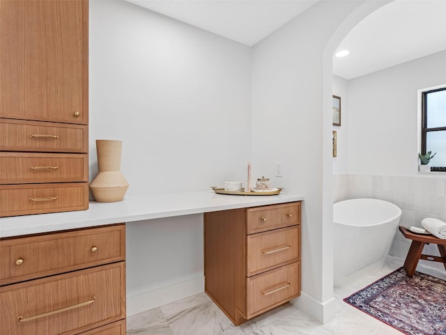 bathroom with a freestanding tub, wainscoting, baseboards, and marble finish floor