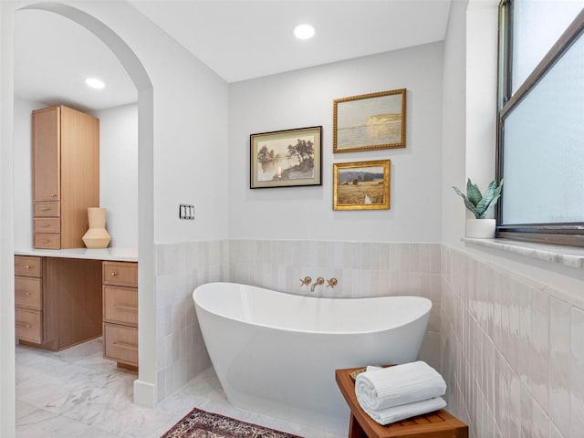 full bathroom featuring a freestanding bath, tile walls, wainscoting, marble finish floor, and recessed lighting