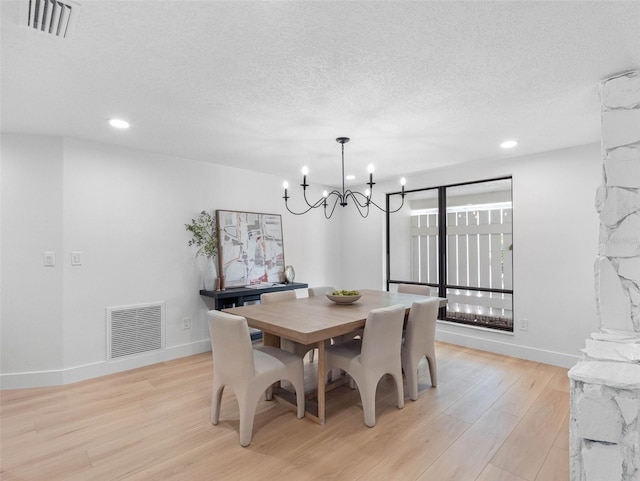 dining room with a textured ceiling, visible vents, an inviting chandelier, and light wood-style floors