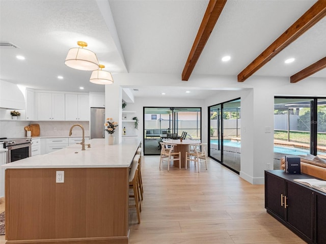kitchen with open shelves, a sink, beam ceiling, stainless steel appliances, and light wood-type flooring