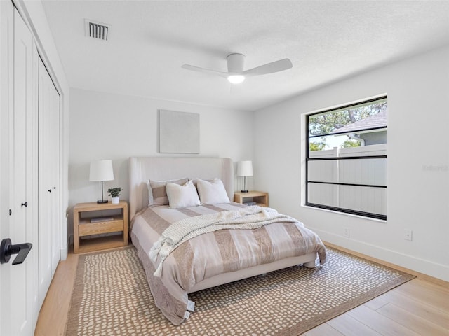 bedroom with ceiling fan, visible vents, light wood finished floors, and a closet