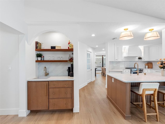 kitchen with light countertops, white cabinetry, custom range hood, a sink, and backsplash