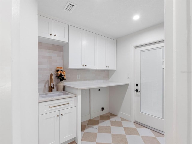 clothes washing area featuring electric dryer hookup, visible vents, cabinet space, a sink, and light floors