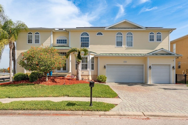 view of front of house with decorative driveway, metal roof, a front lawn, and a garage