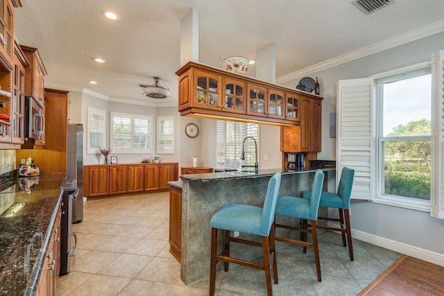 kitchen featuring visible vents, ornamental molding, a kitchen breakfast bar, and brown cabinets
