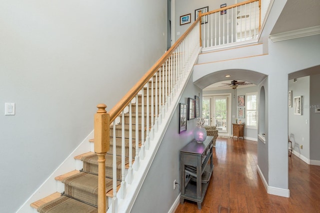 staircase with baseboards, wood-type flooring, arched walkways, a ceiling fan, and a high ceiling