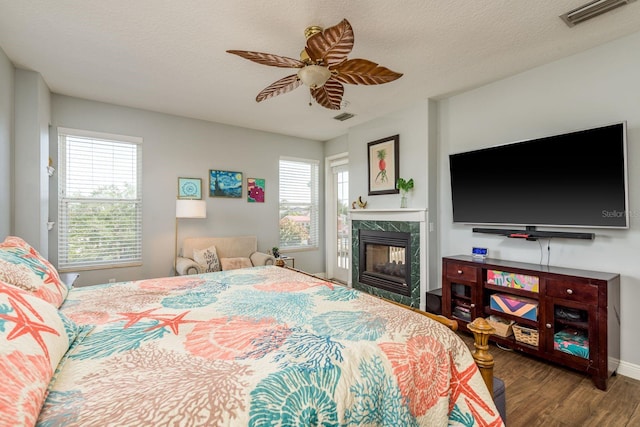 bedroom with a premium fireplace, a ceiling fan, visible vents, and wood finished floors