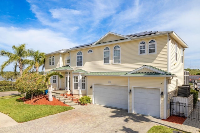 view of front of property with roof mounted solar panels, metal roof, decorative driveway, an attached garage, and fence