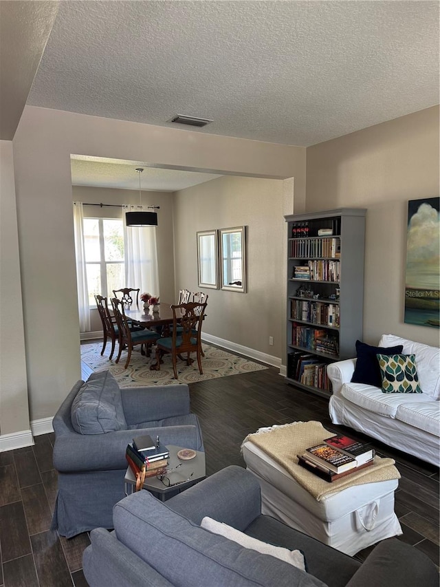 living room with a textured ceiling, baseboards, visible vents, and wood finished floors