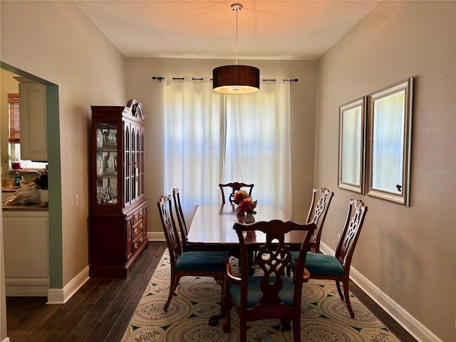dining space with a textured ceiling, baseboards, and dark wood finished floors