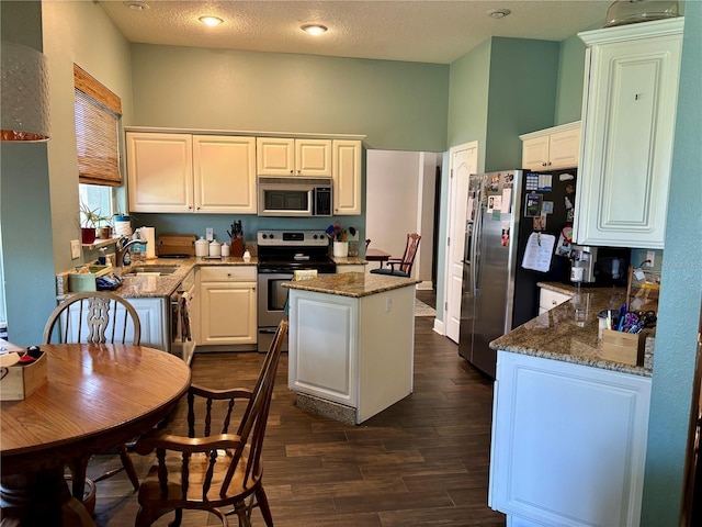 kitchen with a sink, a center island, stainless steel appliances, stone counters, and dark wood-type flooring