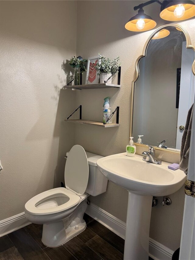 half bathroom with toilet, baseboards, and wood finished floors