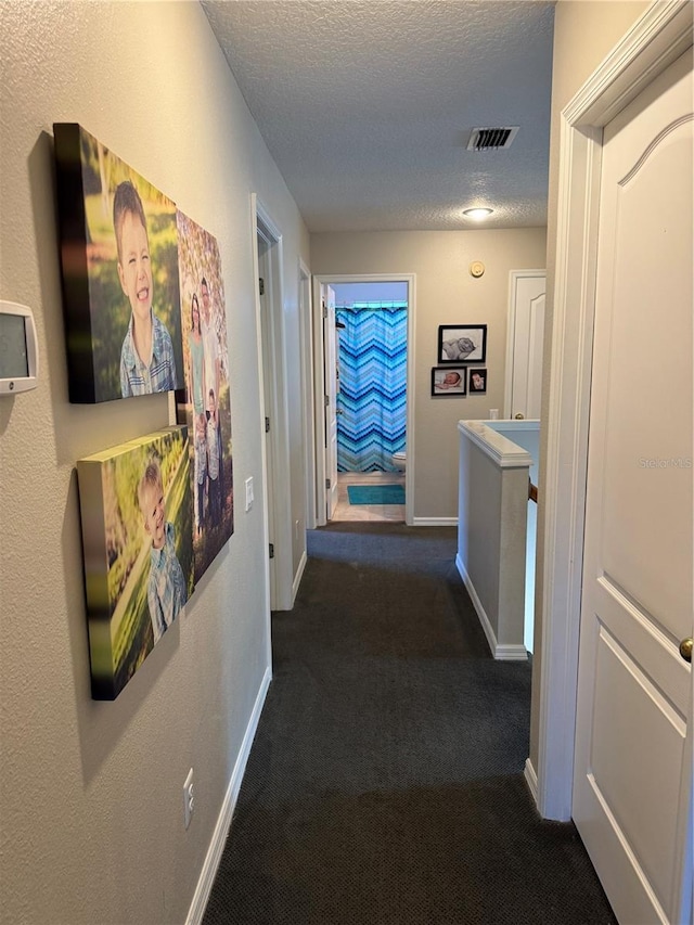 hall with baseboards, dark colored carpet, a textured ceiling, and visible vents