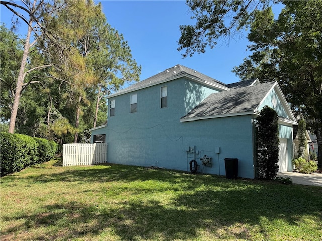 view of side of home featuring fence, a shingled roof, a yard, and stucco siding