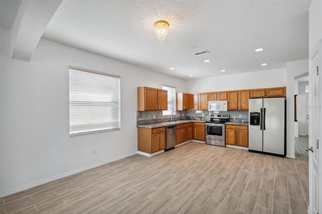 kitchen featuring brown cabinets, a sink, appliances with stainless steel finishes, visible vents, and baseboards
